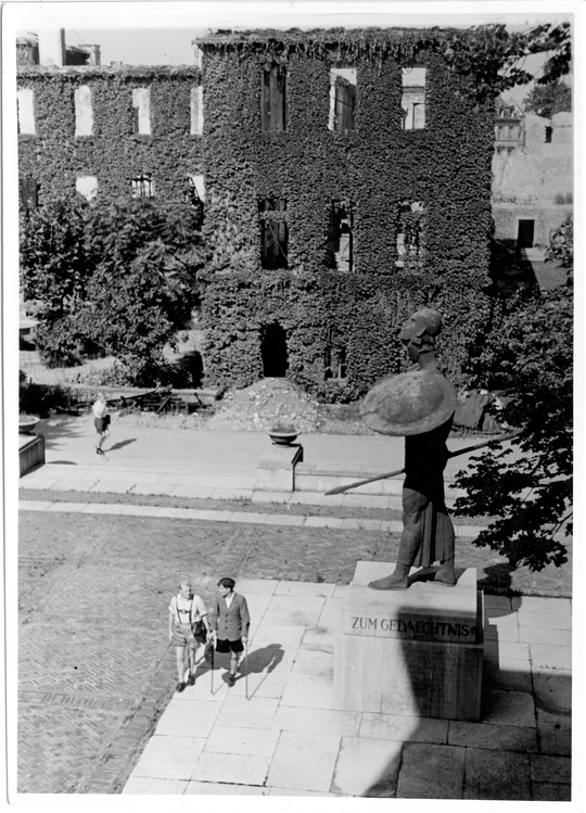 Blick von Osten über den Ehrenhof der Technischen Hochschule Karlsruhe auf den zerstörten Westflügel des Hauptgebäudes und das Denkmal für die Gefallenen des ersten Weltkriegs, neben diesem zwei Kriegsversehrte, ca. 1947, Fotografie: Erich Bauer. KIT-Archiv 28010/I 3923.