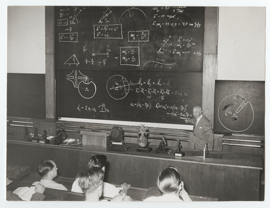Otto Kraemer (Prof. für Kolbenmaschinen), in der Vorlesung "Getriebelehre" im Grashof-Hörsaal, auf dem Pult Modelle der Redtenbacher-Sammlung, ca. 1950, Fotografie unbekannter Urheberschaft. KIT-Archiv 28010/I 3211.